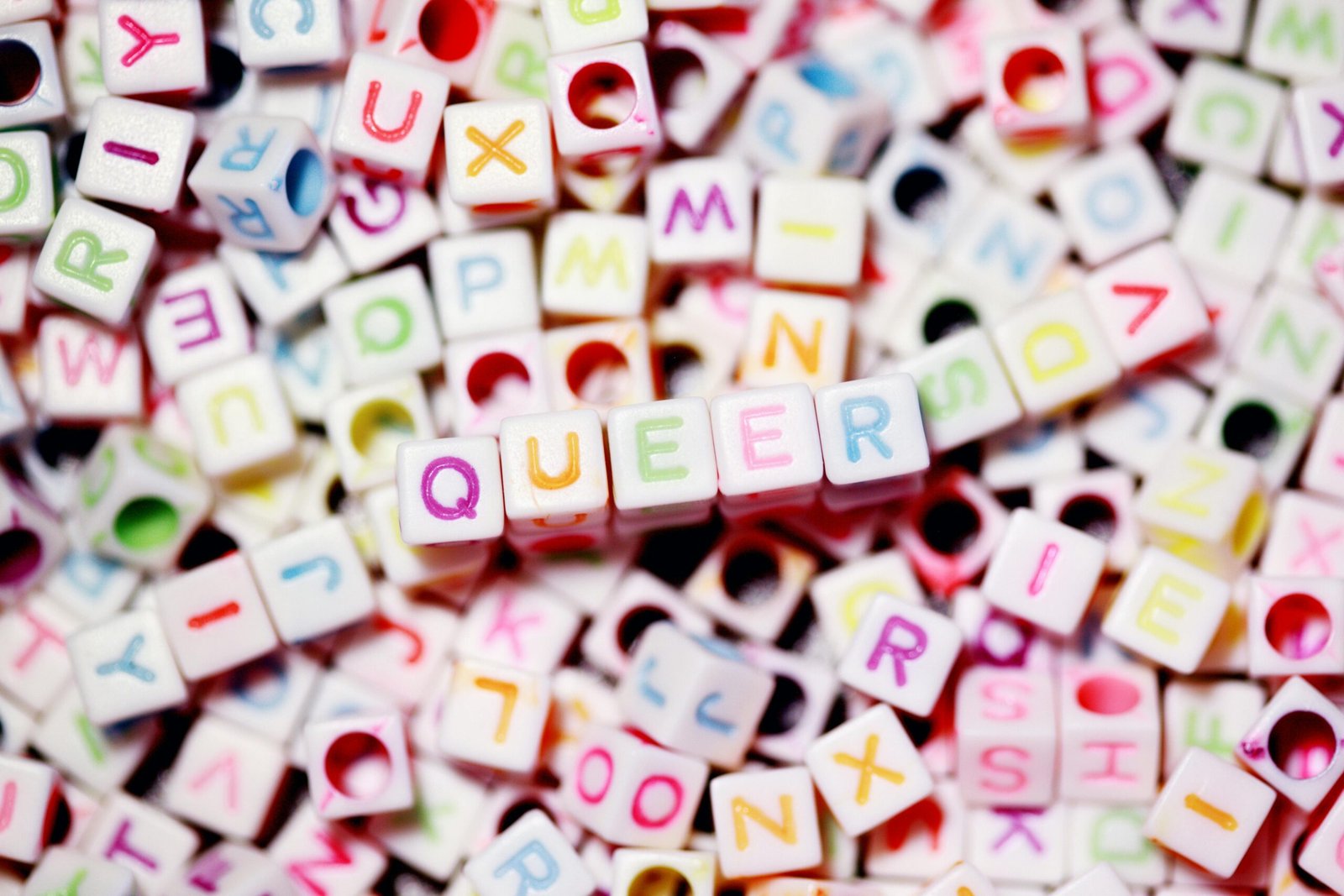 Close-up of colorful alphabet beads spelling out 'QUEER' on a blurred background.